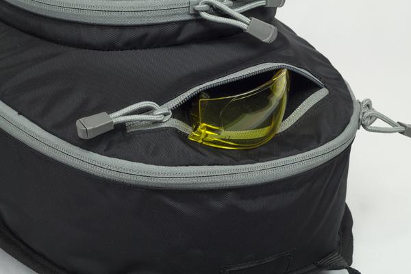 Close-up of an Elite Survival Systems Gen II Smokescreen Backpack with a zipper partially open, revealing yellow safety goggles inside.