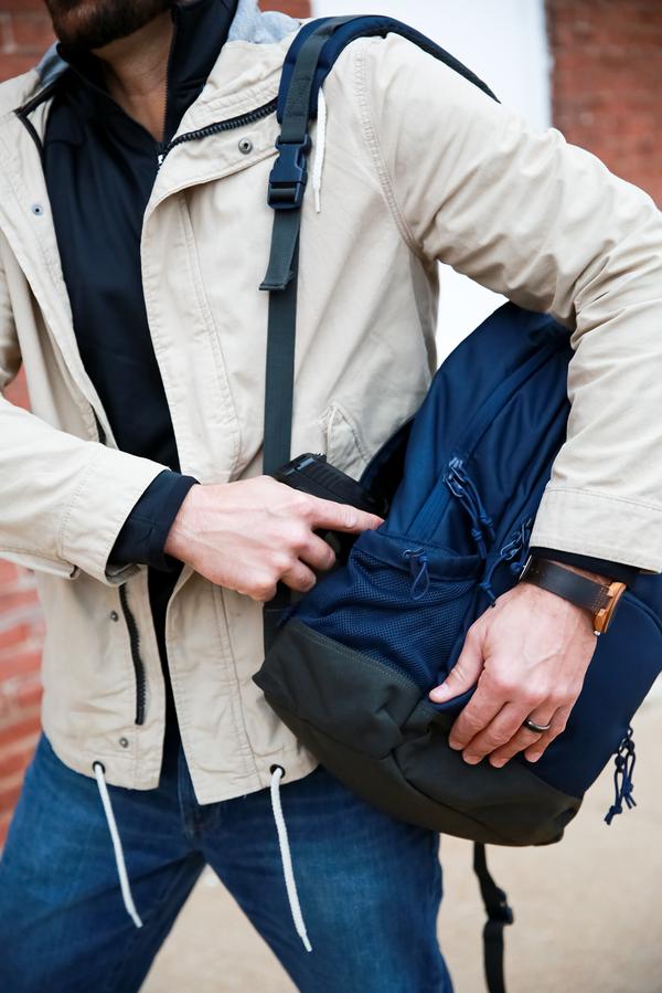 Man in a beige jacket reaching into his blue Elite Survival Systems Echo EDC Backpacks 7721-TR.