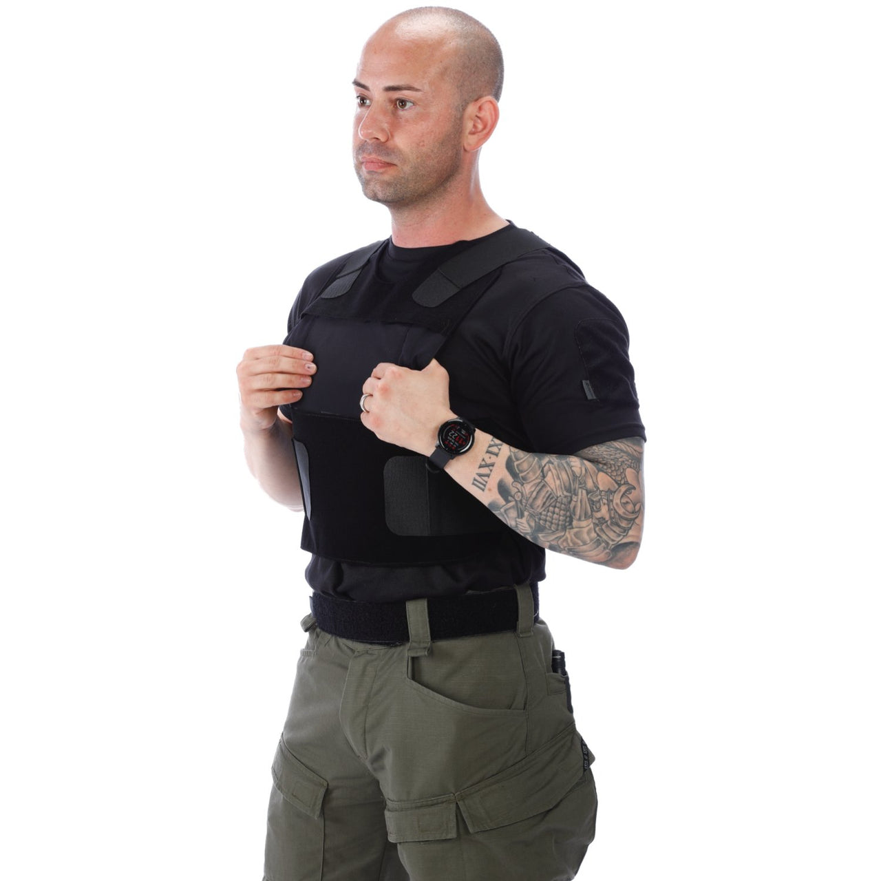 A man in a green shirt and black pants is posing in front of a white background wearing the Body Armor Direct All American Concealable Enhanced Multi-Threat Vest by Body Armor Direct.