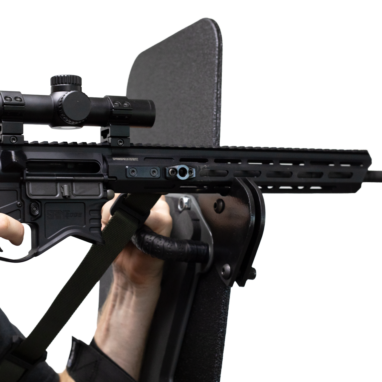 Close-up of a rifle with a scope resting on a support bracket that is mounted to a bulletproof shield