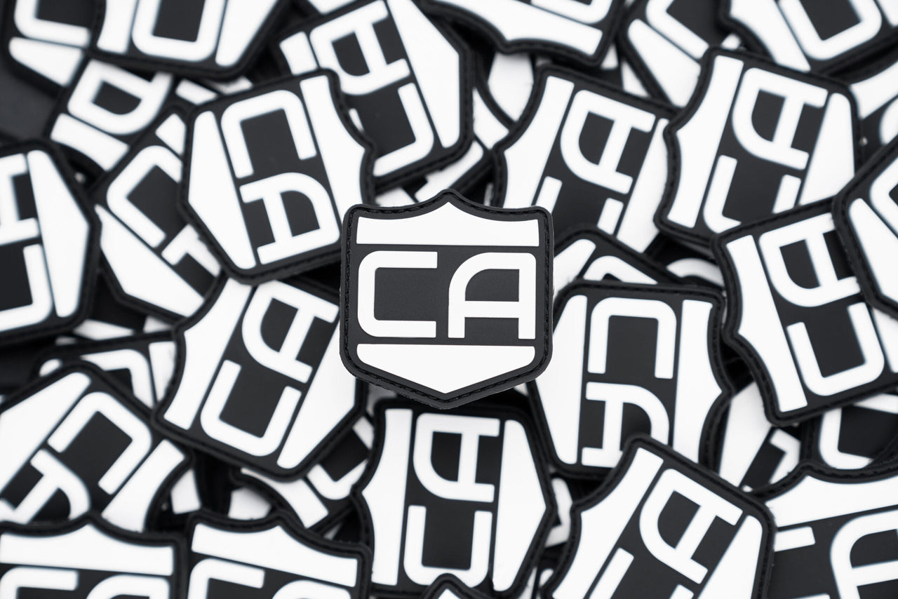A stack of black and white Caliber PVC Morale Patches by Caliber Armor features bold "CA" lettering—perfect for adding a tactical touch to your gear.
