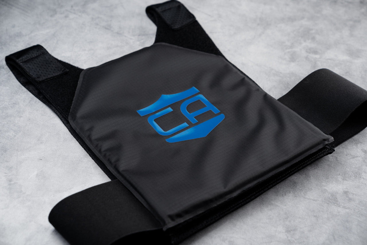 The Caliber Armor CaliberX IIIA Gray Man Concealable Package bulletproof vest, featuring a blue shield logo, is laid flat on a gray surface.