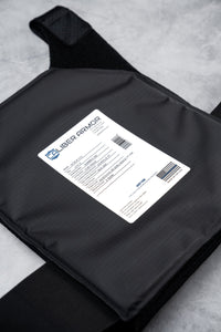 Thumbnail for A close-up of a Caliber Armor CaliberX IIIA Gray Man Concealable Package body armor plate with a white product info label and barcode, shown on a light gray surface.