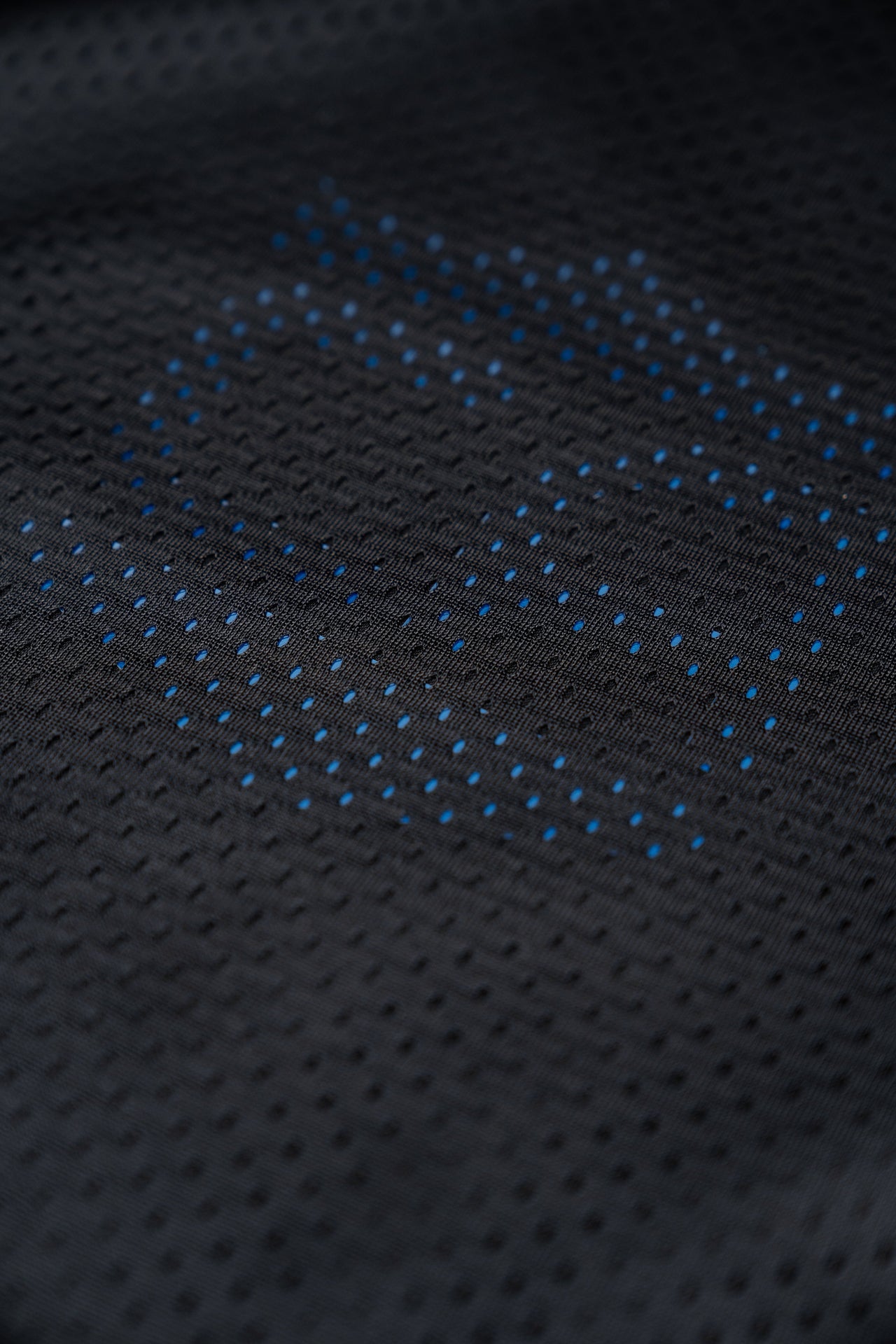 Close-up of the Gray Man Concealable Carrier from Caliber Armor, featuring black perforated fabric with a blue hexagonal dotted pattern—ideal for discreet wear or soft armor panels.