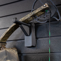 Thumbnail for close up of black plastic hanger for compound bow shown mounted to a black tactical gear slat wall named Assault Wall with a cammo bow hung from the upper limb