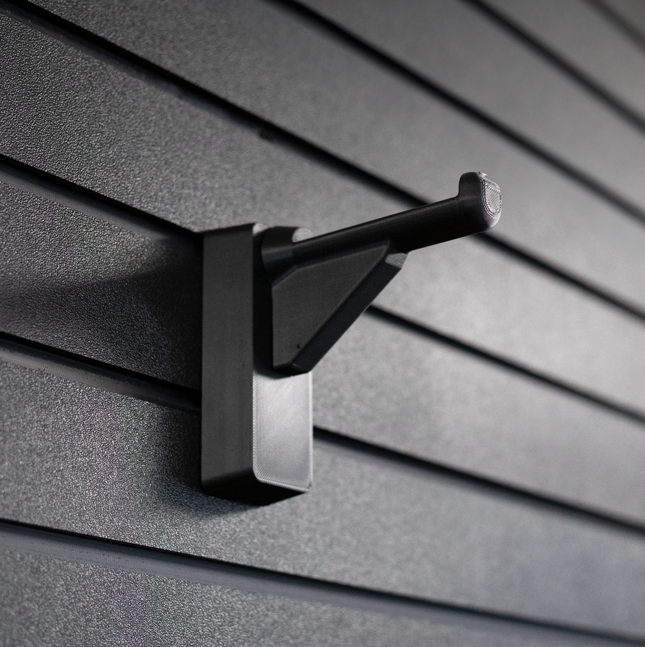 black plastic hanger for compound bows and crossbows shown mounted to a black tactical gear slat wall named Assault Wall