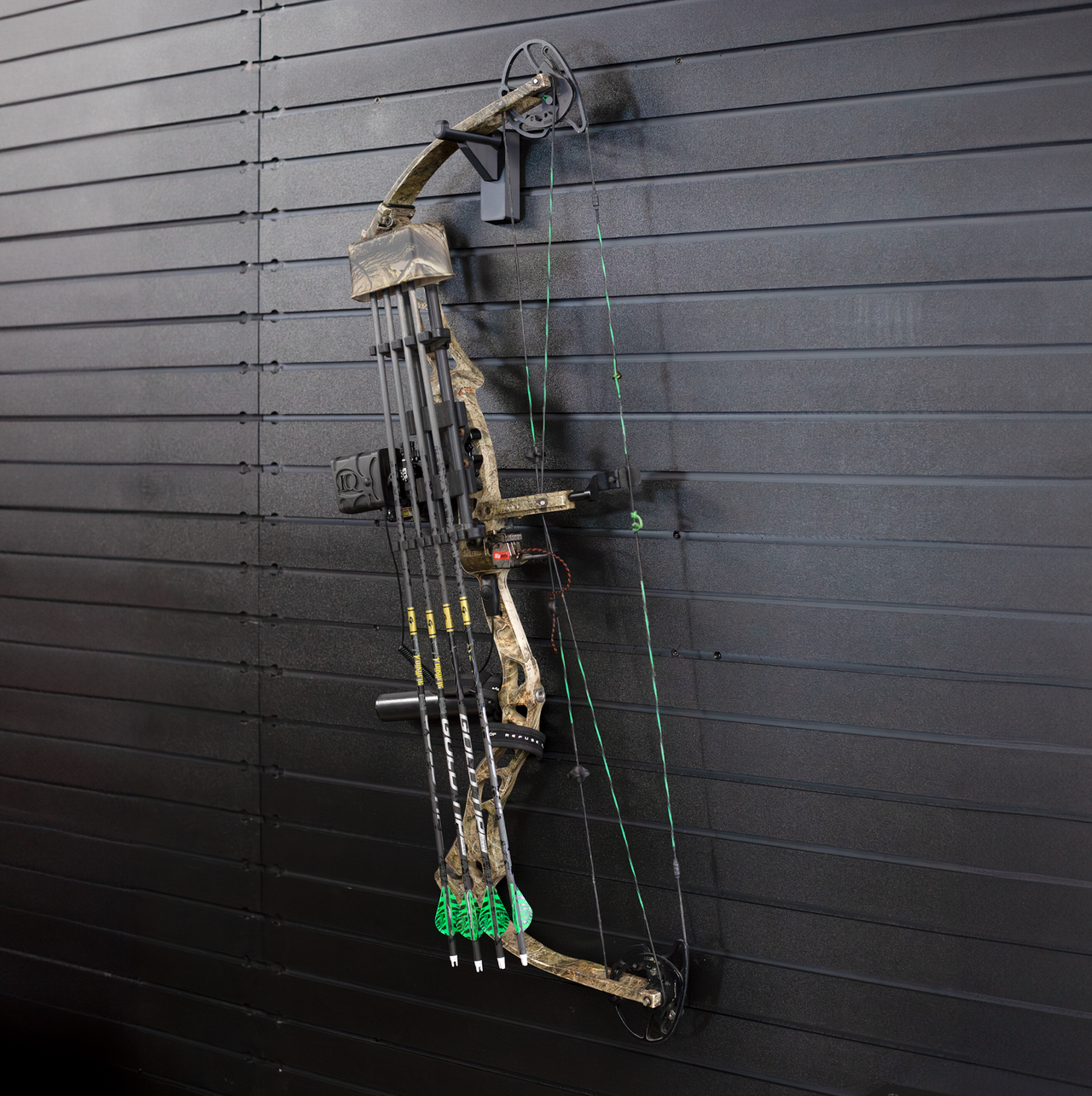 full view of black plastic hook hanger for compound bow shown mounted to a black tactical gear slat wall named Assault Wall with a cammo bow hung from the upper limb of the bow