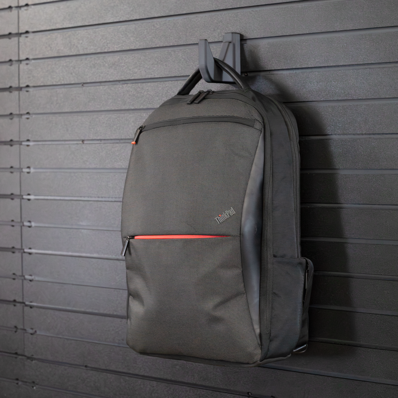 Black single hook mounted to the Assault Wall slat wall panel system  hook is holding a backpack