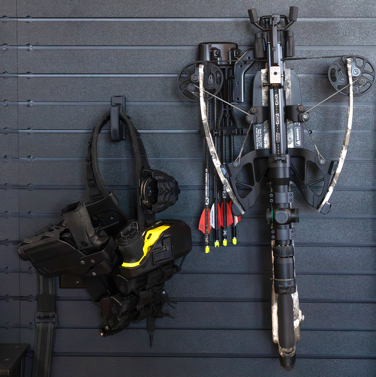 Compound bow and loaded law enforcement duty belt both hung from black plastic hooks on slat wall