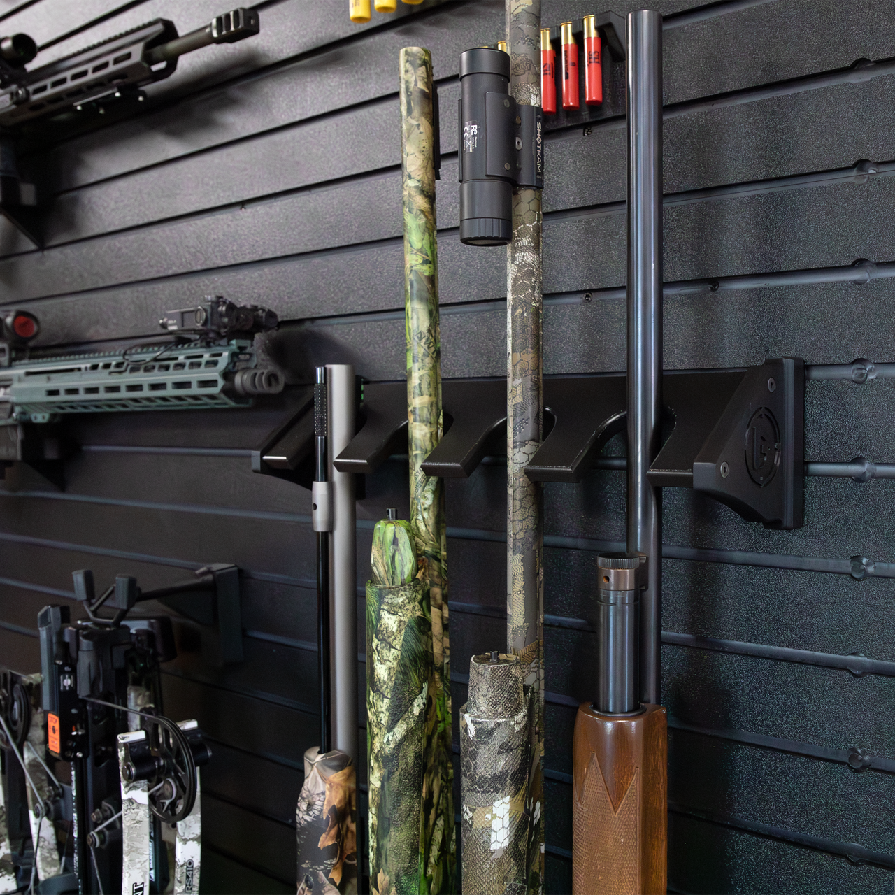Close up of black plastic vertical four gun storage mount, shown with barrels of long guns shown retained in upper portion of the mount, they are mounted to our black  Assault Wall slat wall paneling