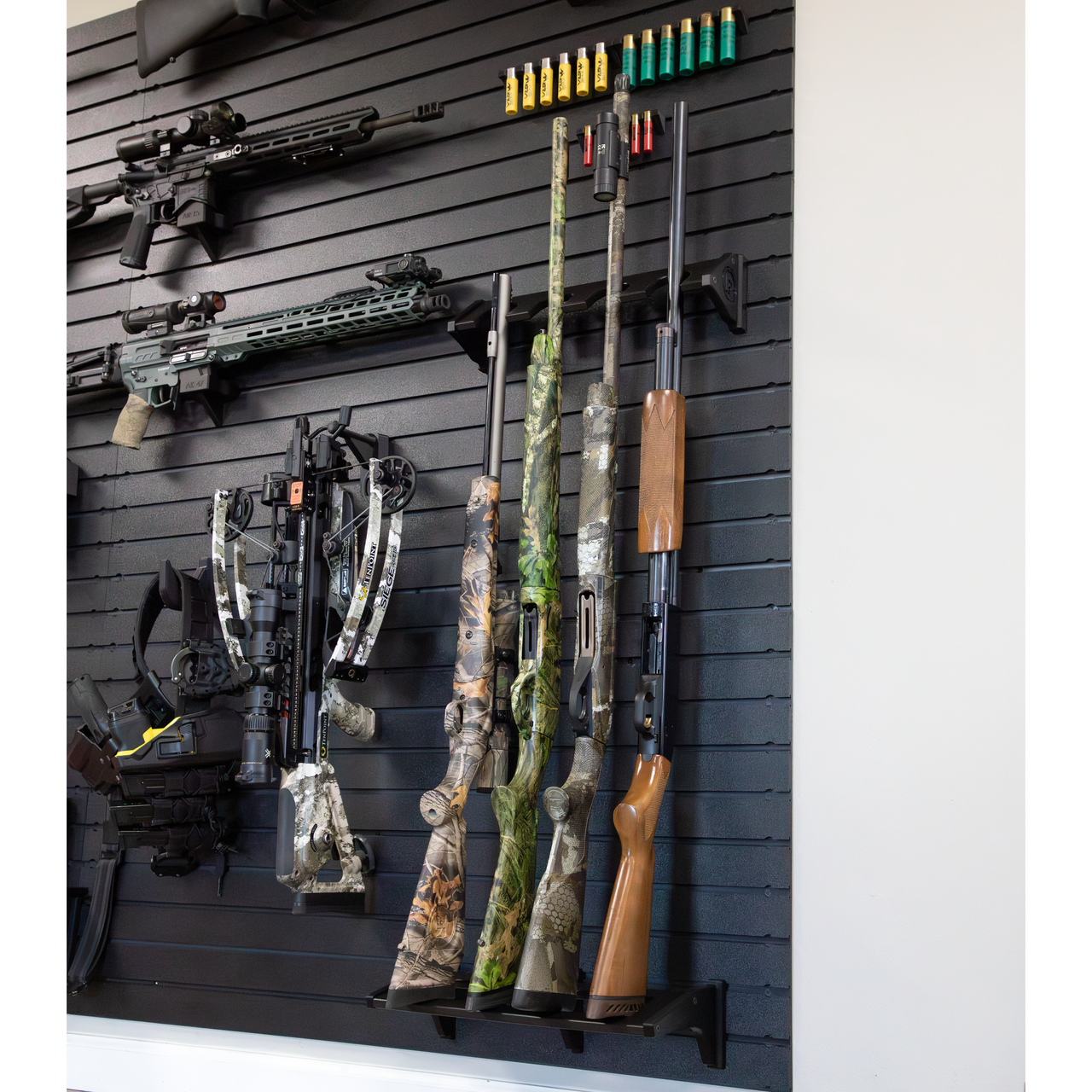 Black plastic vertical four gun storage mount, both upper & lower portion of mount shown mounted to our black  Assault Wall slat wall paneling loaded with shotguns & muzzelloaders with other tactical gear and guns shown mounted surrounding the mount