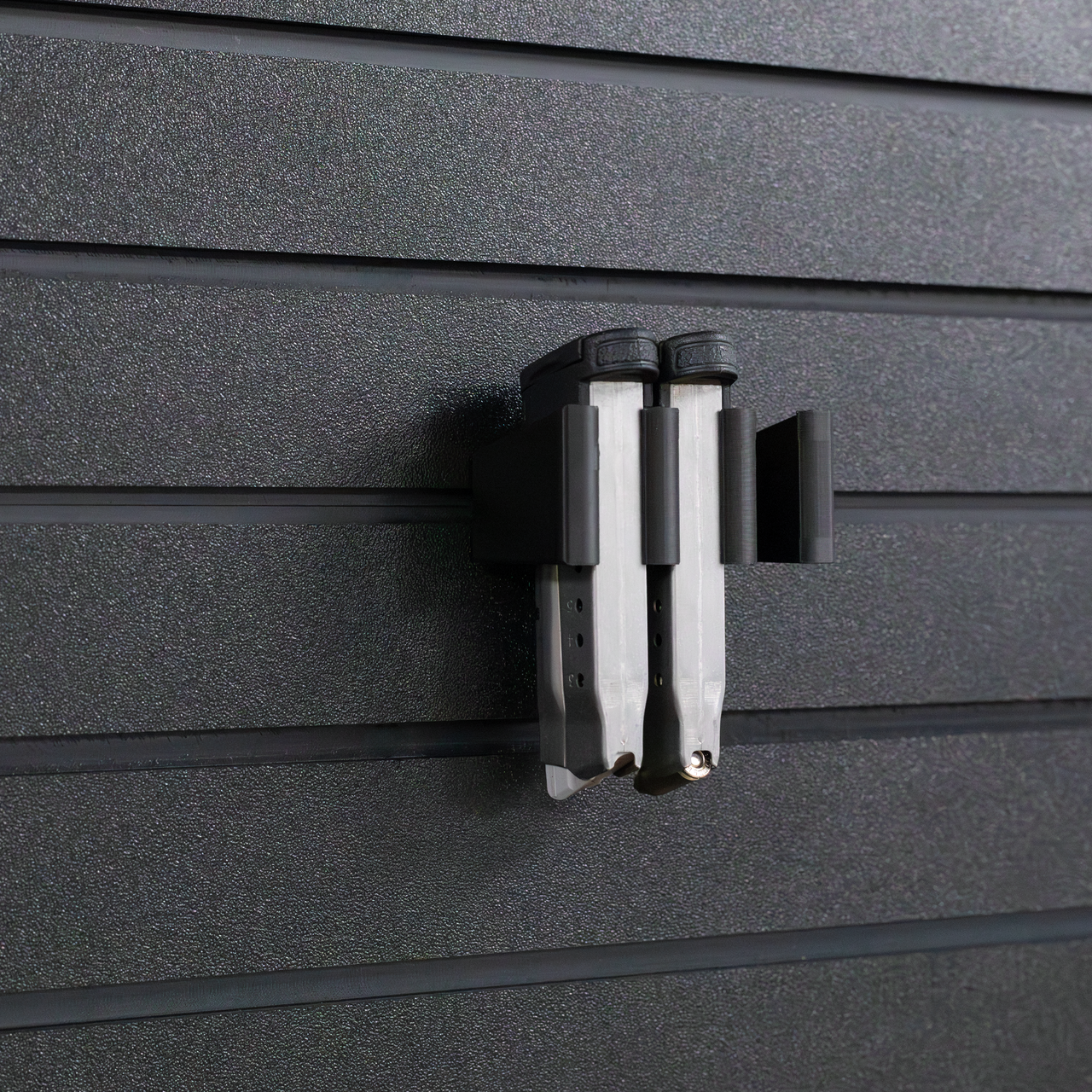 Black pistol magazine hanger showing two 9mm single stack slim magazines installed into mount and hung on an Assault Wall tactical slat wall panel, 3 magazine capacity