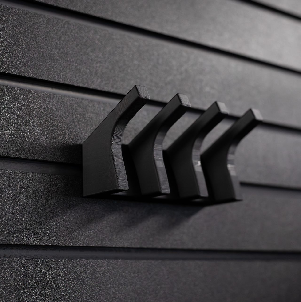 Black AK-47 magazine hanger, installed on an Assault Wall tactical slat wall, close up view showing the hanger without rifle magazines installed or hanging