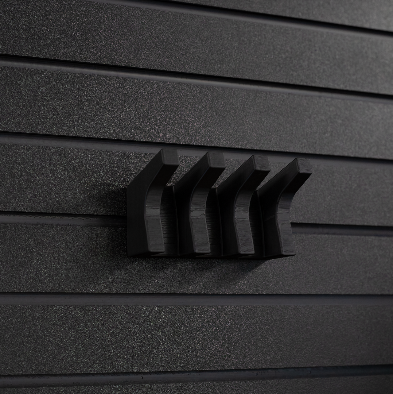 Black AR-15 magazine hanger, installed on an Assault Wall tactical slat wall, close up view showing the hanger without rifle magazines installed or hanging