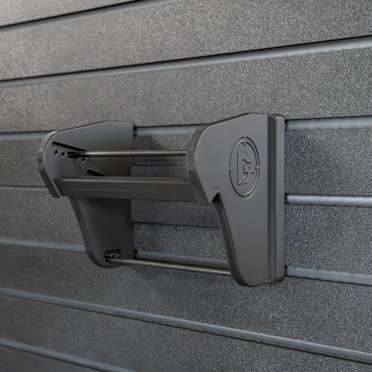Assault Wall Universal Mag Holder with doublet tap logo with adjustable tension, shown empty mounted to a black Assault Wall panel, highlighting the adjustable slot options that the carbon fiber rod rests in