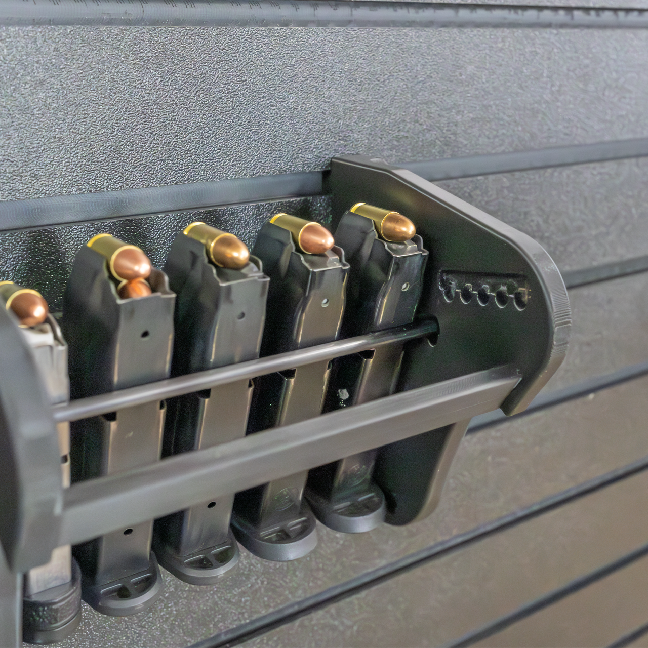 Assault Wall Universal Mag Holder with adjustable tension, shown loaded with pistol mags organized & mounted to a black Assault Wall panel, highlighting the adjustable slot options that the carbon fiber rod rests in