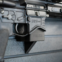 Thumbnail for Close-up of an AR-15 rifle mounted by its magazine well on an Assault wall caliber specific gun mount installed on a slat wall