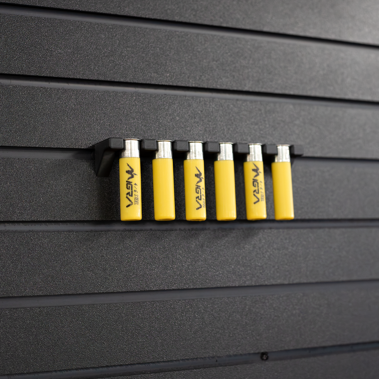 Six yellow 20 gauge shotgun shells hanging from a black mount that is attached to an Assault Wall tactical slat wall panel