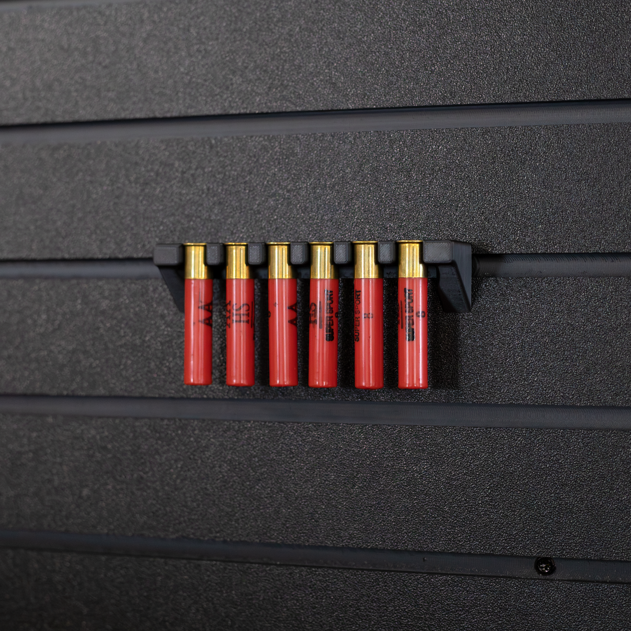 Six red .410 shotgun shells hanging from a black mount that is attached to an Assault Wall tactical slat wall panel
