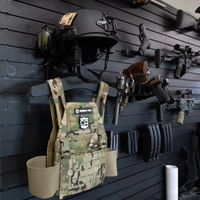 Thumbnail for Loaded black plastic plate carrier and helmet hanging system for duty or  tactical gear mounted to Assault Wall slat wall with guns and accessories organized in the blurred background
