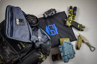Thumbnail for A tactical backpack, earmuffs, camera, black mat with blue logo, green handgun, green folding knife, holster, ammo pouch, and a Caliber Armor CaliberX IIIA Body Armor Insert for Haley Strategic Backpacks are arranged on a light surface.