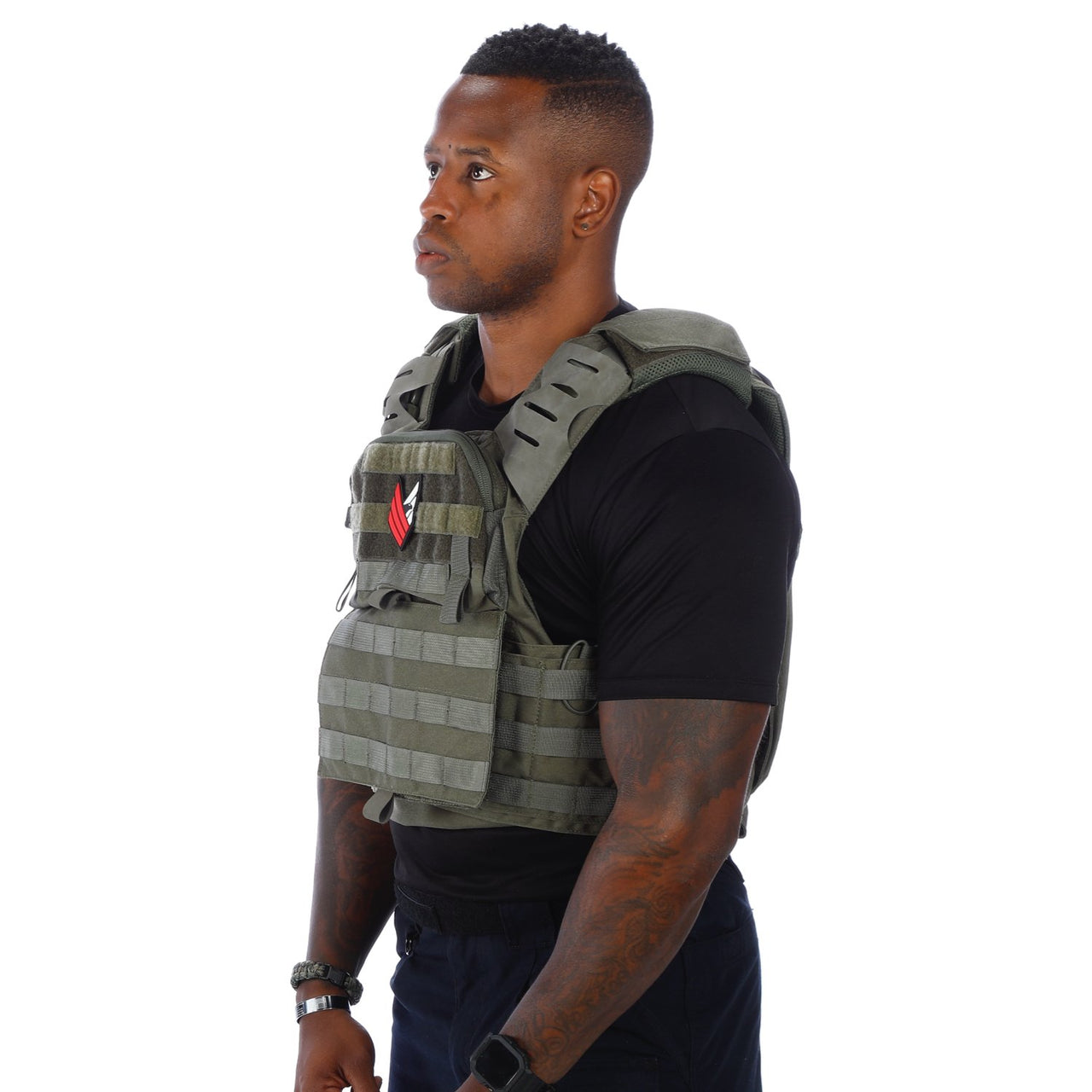 A man in a black shirt and green Body Armor Direct Victory Plate Carrier Deluxe Edition with patches stands in profile against a white background.